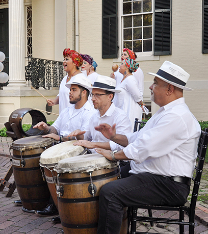 Đoàn múa Tradicion Dancy biểu diễn bên ngoài Tòa nhà điều hành. Ba người đàn ông đang ngồi đánh trống ở phía trước và một nhóm phụ nữ đang hát phía sau họ.